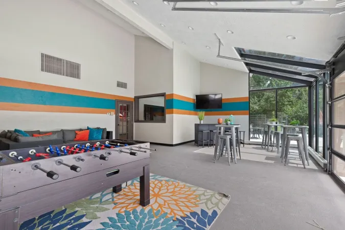 Modern lounge with foosball table, stools, wall-mounted TV, and large glass doors to a patio