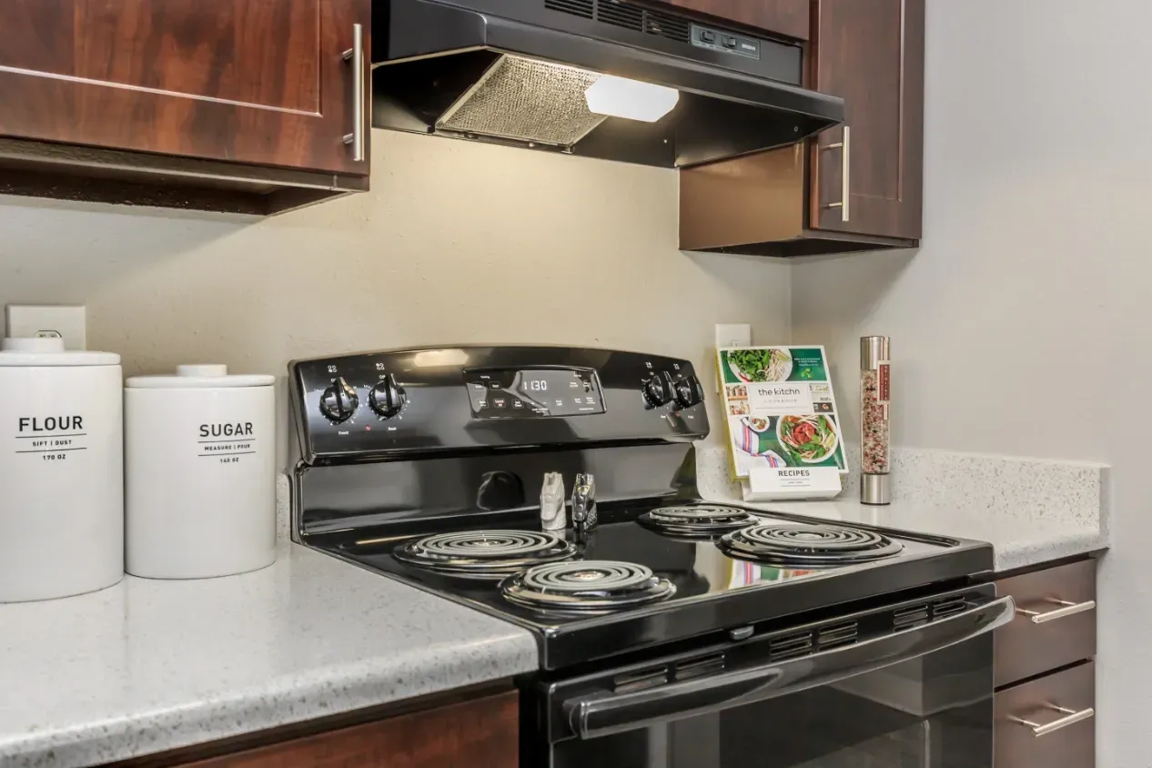 Close-up of a black electric stove in a kitchen, with flour and sugar canisters to the left.