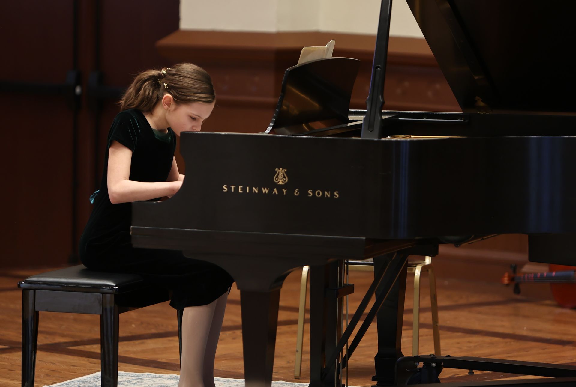 Young person playing a Steinway piano, dark dress, indoor performance setting.