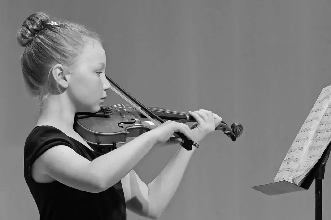 Young person playing a violin, reading music from a stand; black and white.