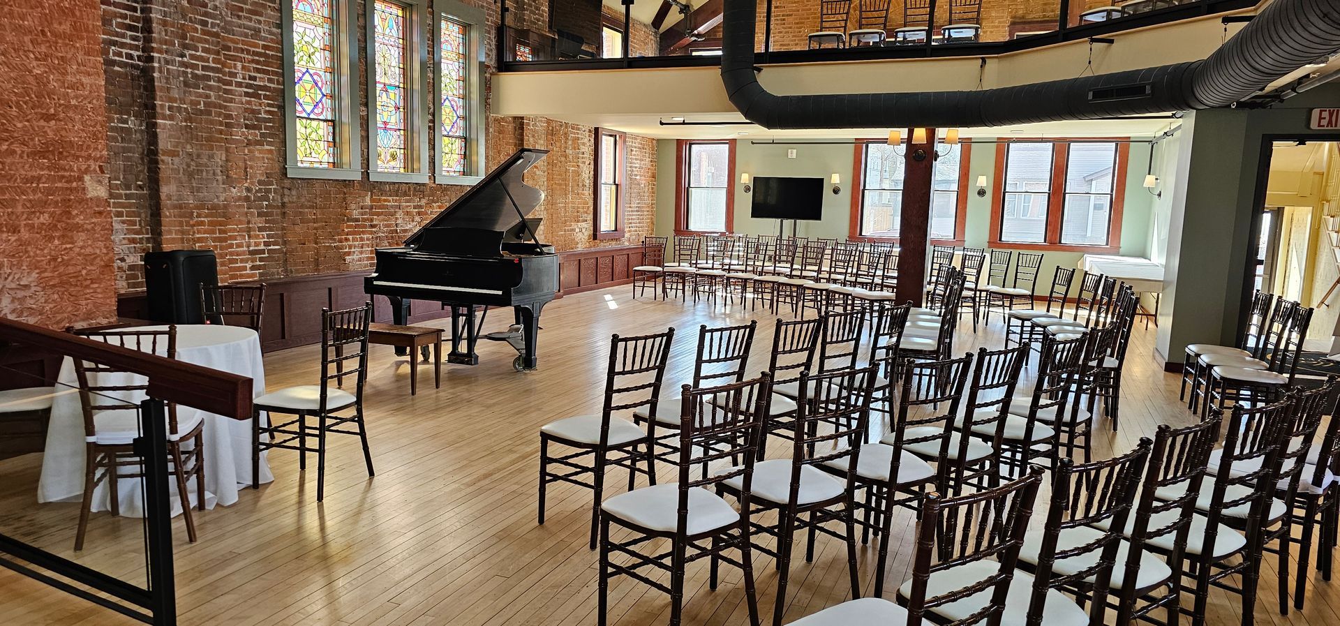 Interior with grand piano, chairs set up in a circular pattern for an event. Exposed brick, wood floor.