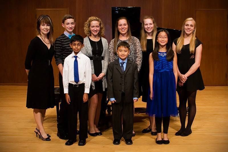 A cello and a smaller viola, both on stands, stand against a wall with a window.
