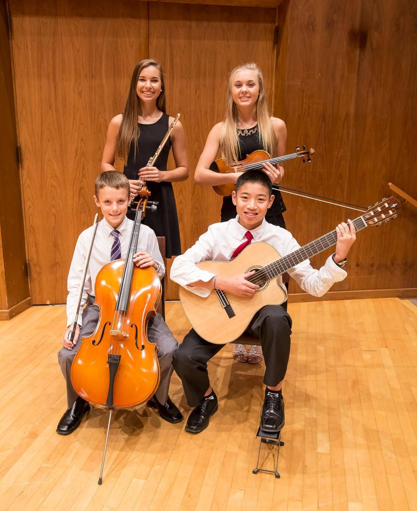 Four young musicians with instruments posing indoors: flute, ukulele, cello, and guitar.