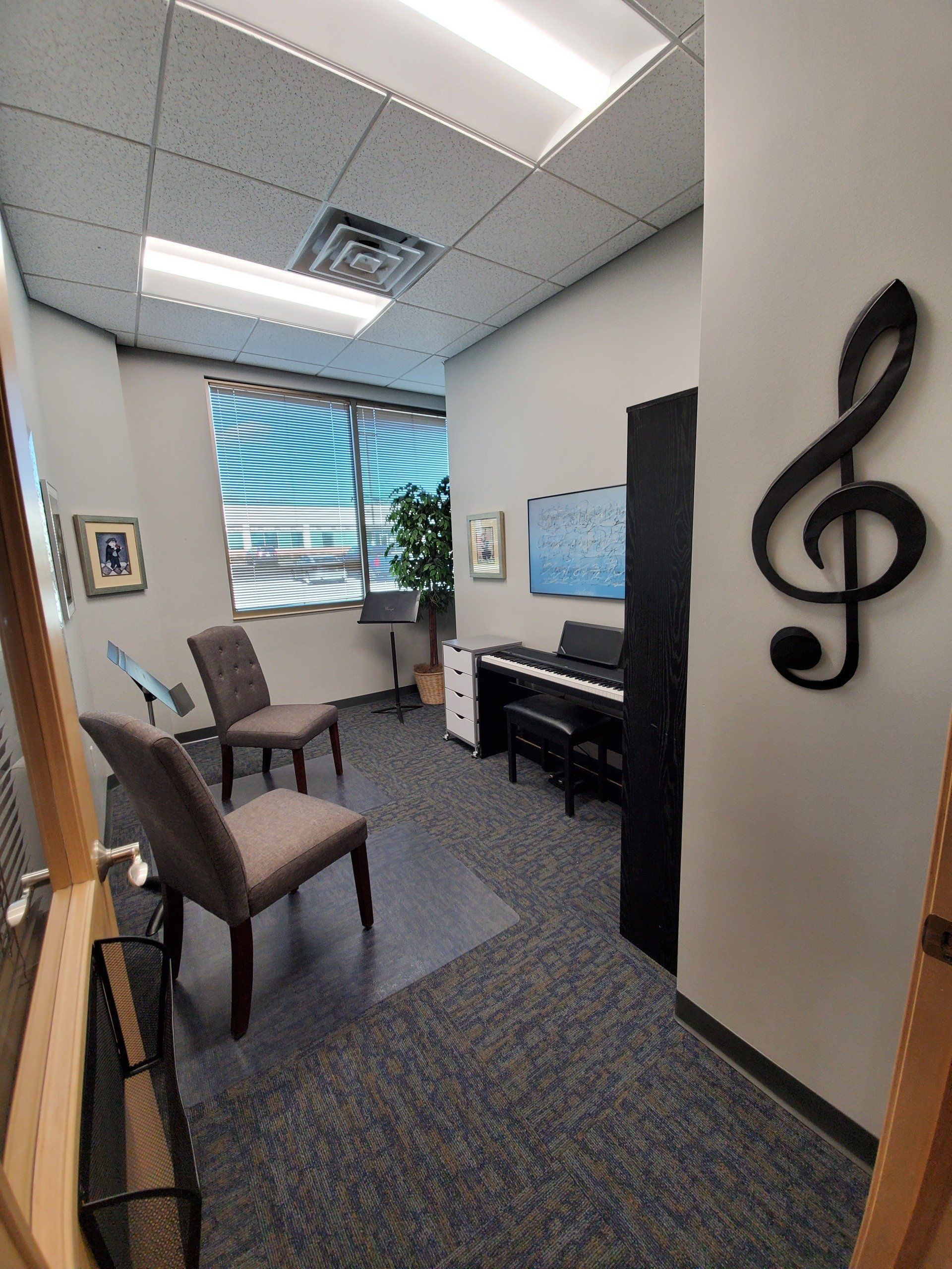Music practice room: piano, chairs, treble clef wall decor, window with blinds.