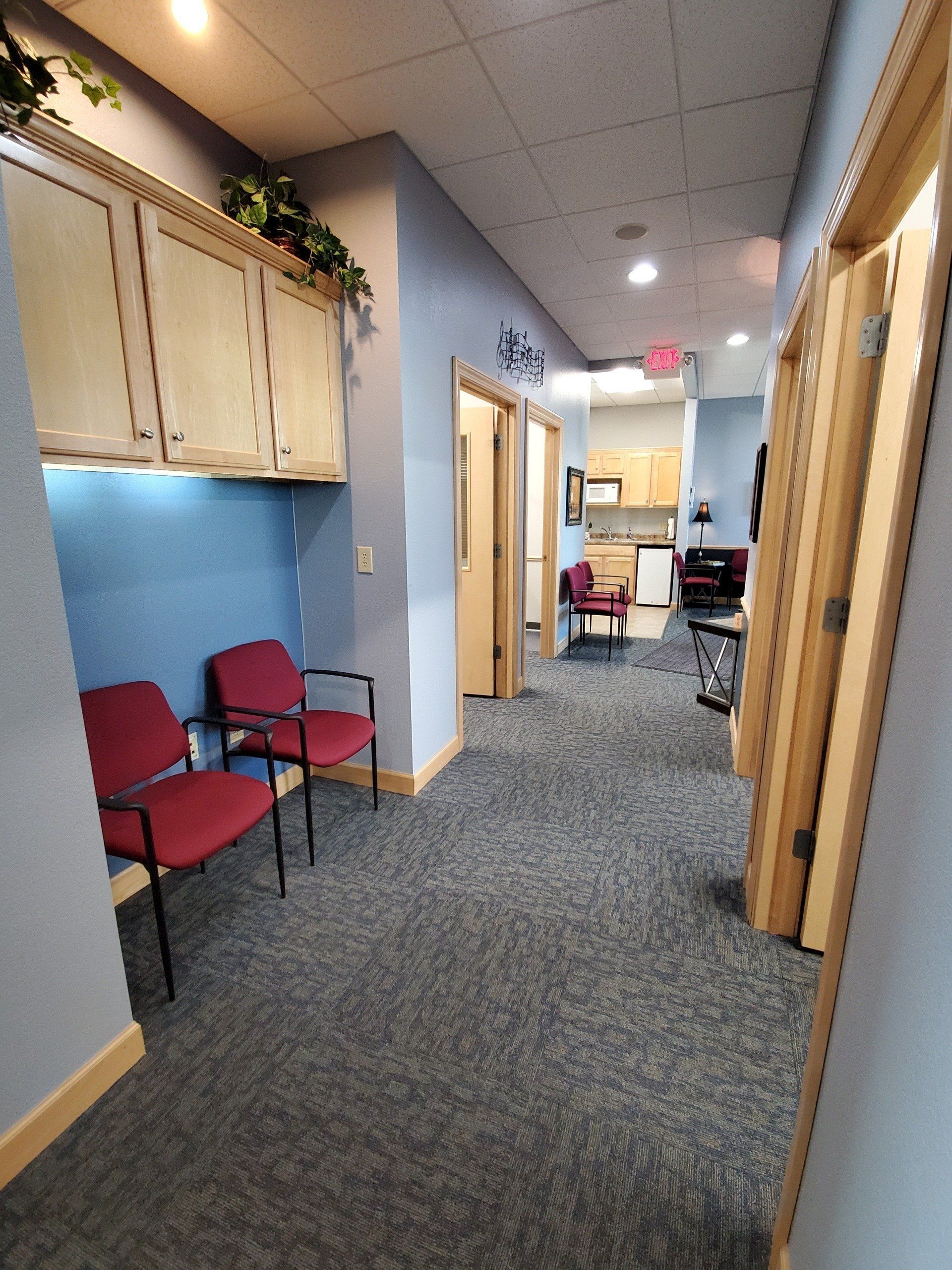 Hallway with blue walls, cabinets, red chairs, and a kitchen visible at the end.