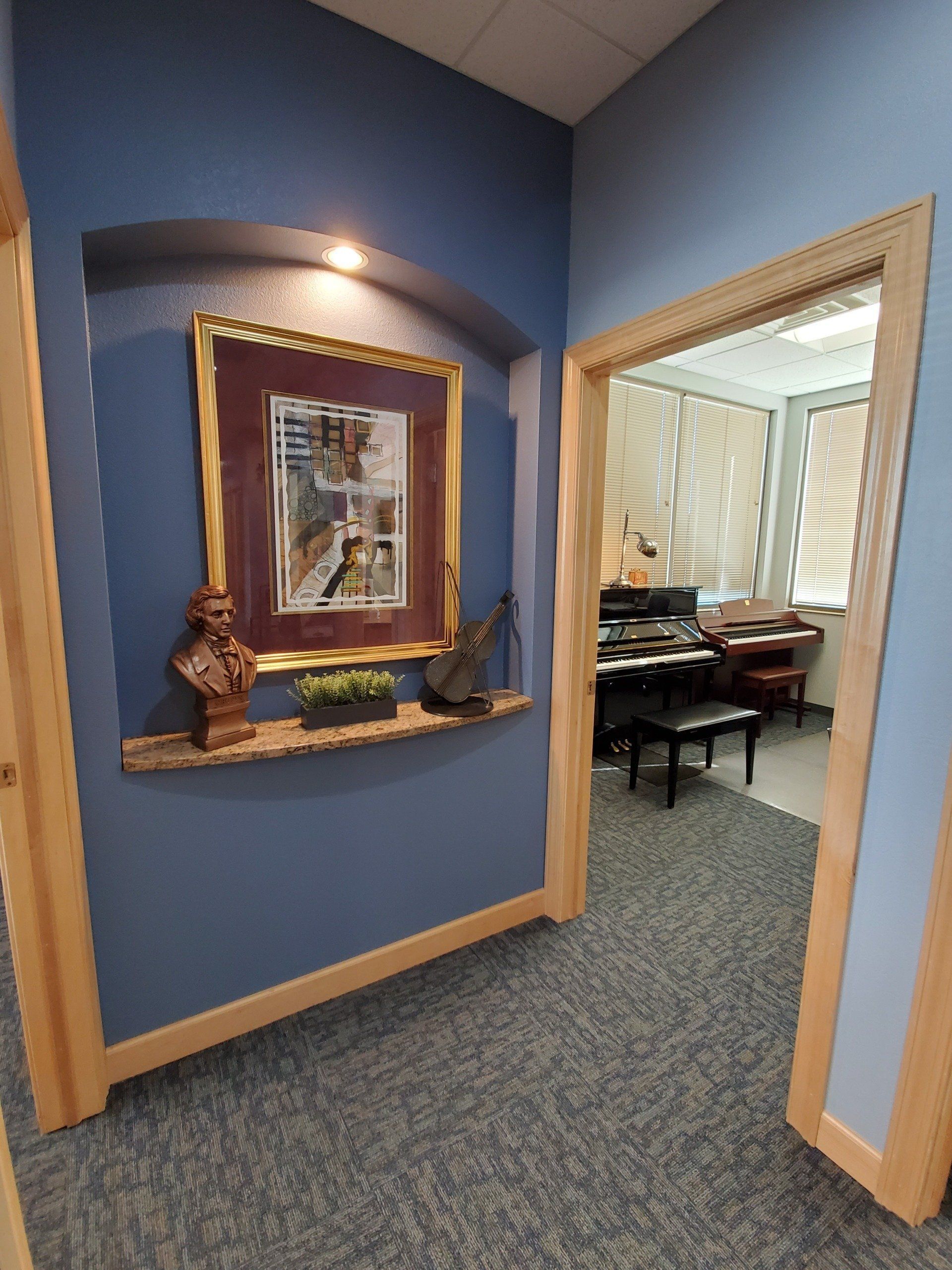 Hallway with a blue accent wall, artwork, and a doorway to an office.