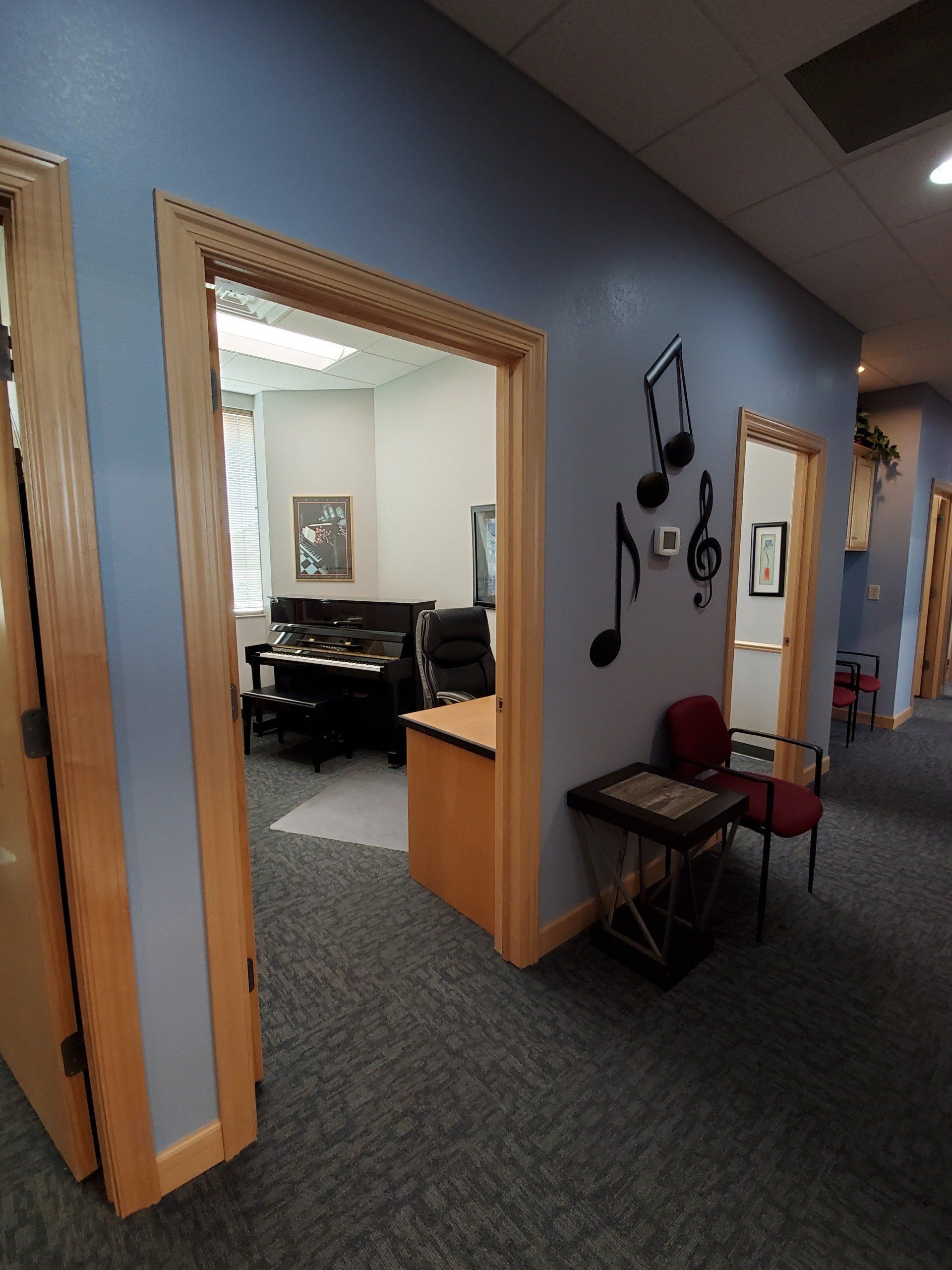 Hallway with blue walls, open doorways to rooms with piano and chair. Music notes on wall.