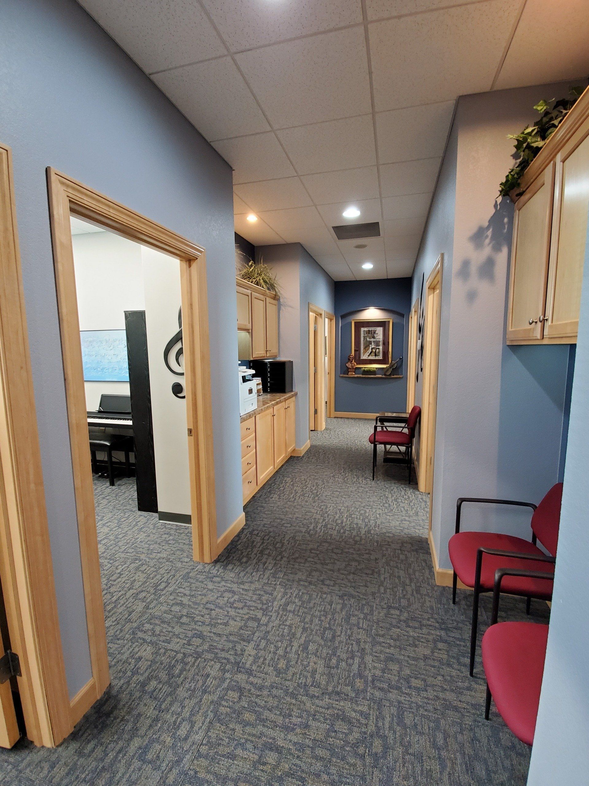 Hallway with blue walls, beige cabinets, and red chairs.