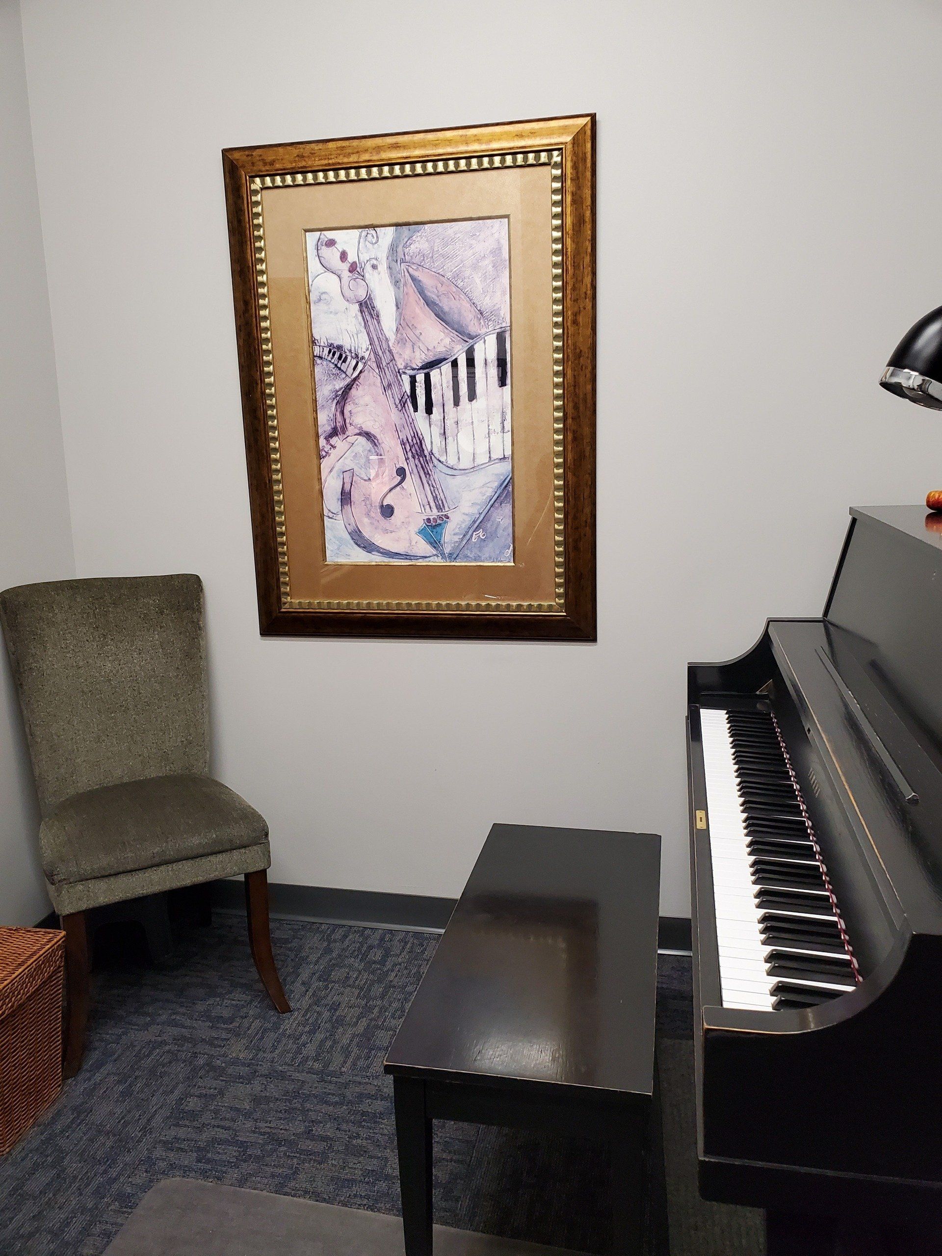 Piano and bench beside a framed artwork and chair in a room with blue carpet.
