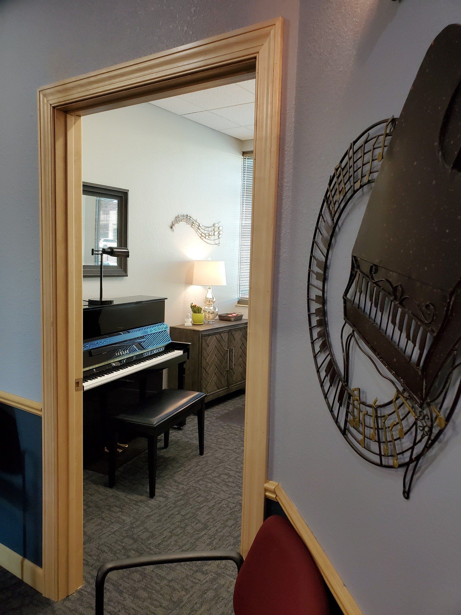 A doorway reveals a music room with a piano, desk, and decorative wall art.