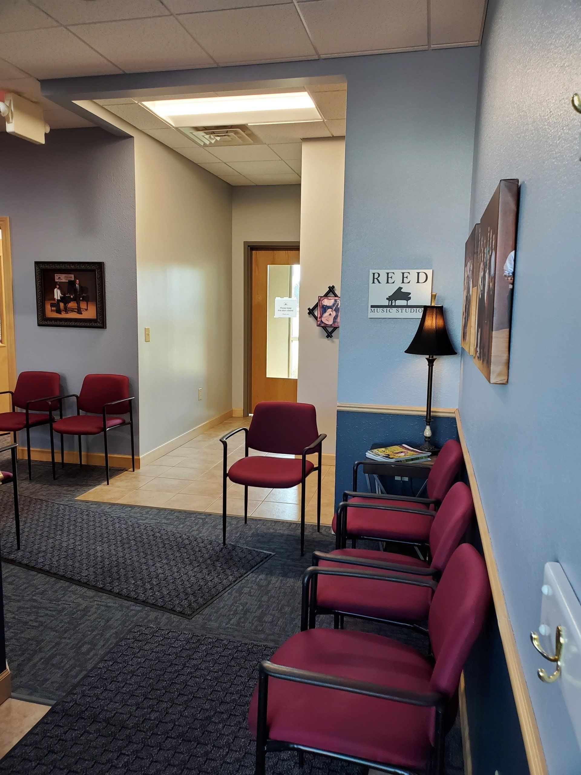 A waiting room with burgundy chairs, blue walls, a dark carpet, and an open hallway.
