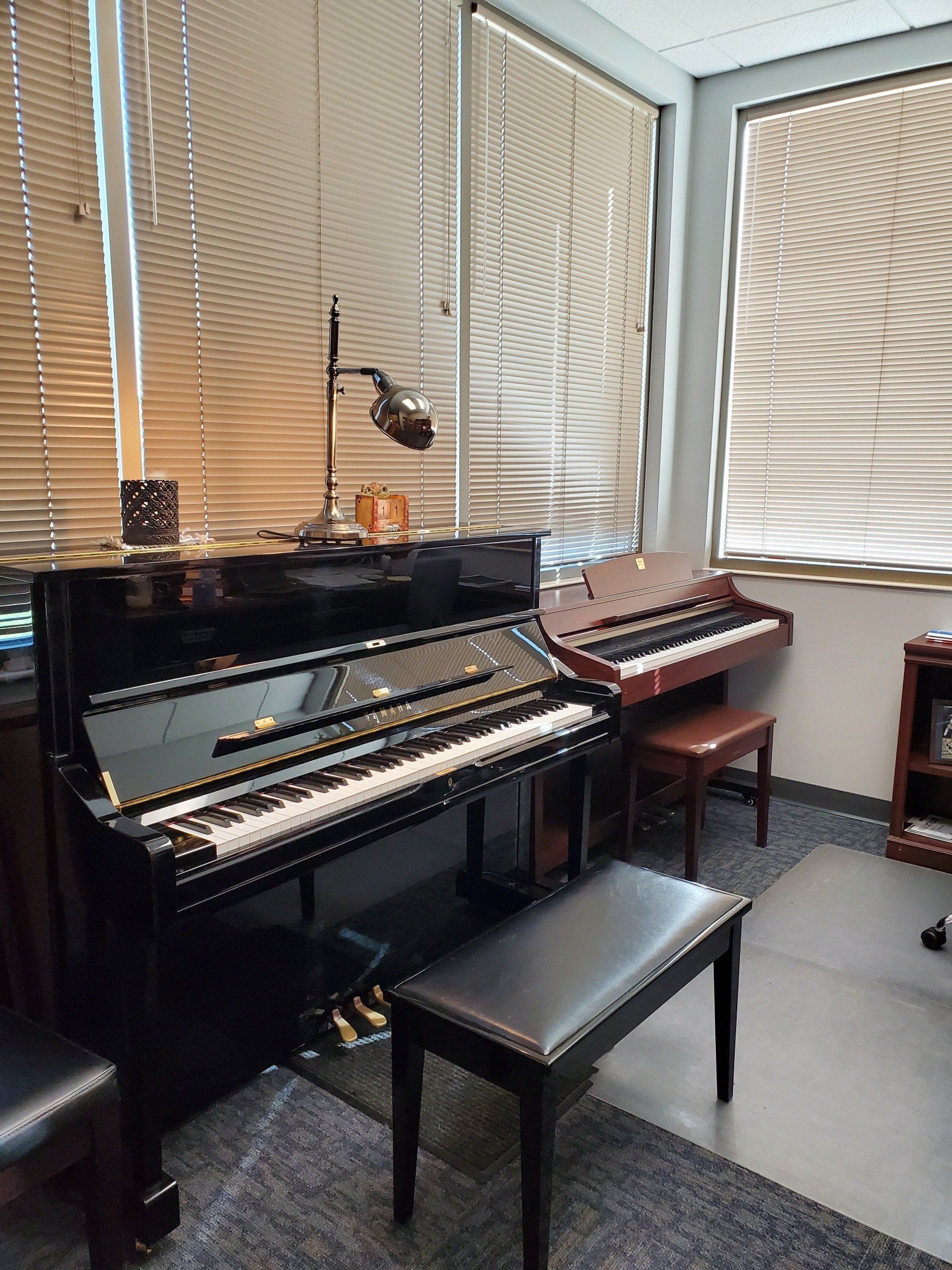 A piano and a smaller organ sit in a room with a window and a piano bench.