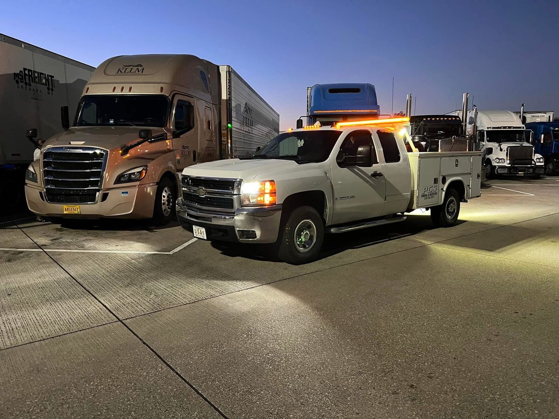 White work truck with orange lights parked near semi-trucks at night.