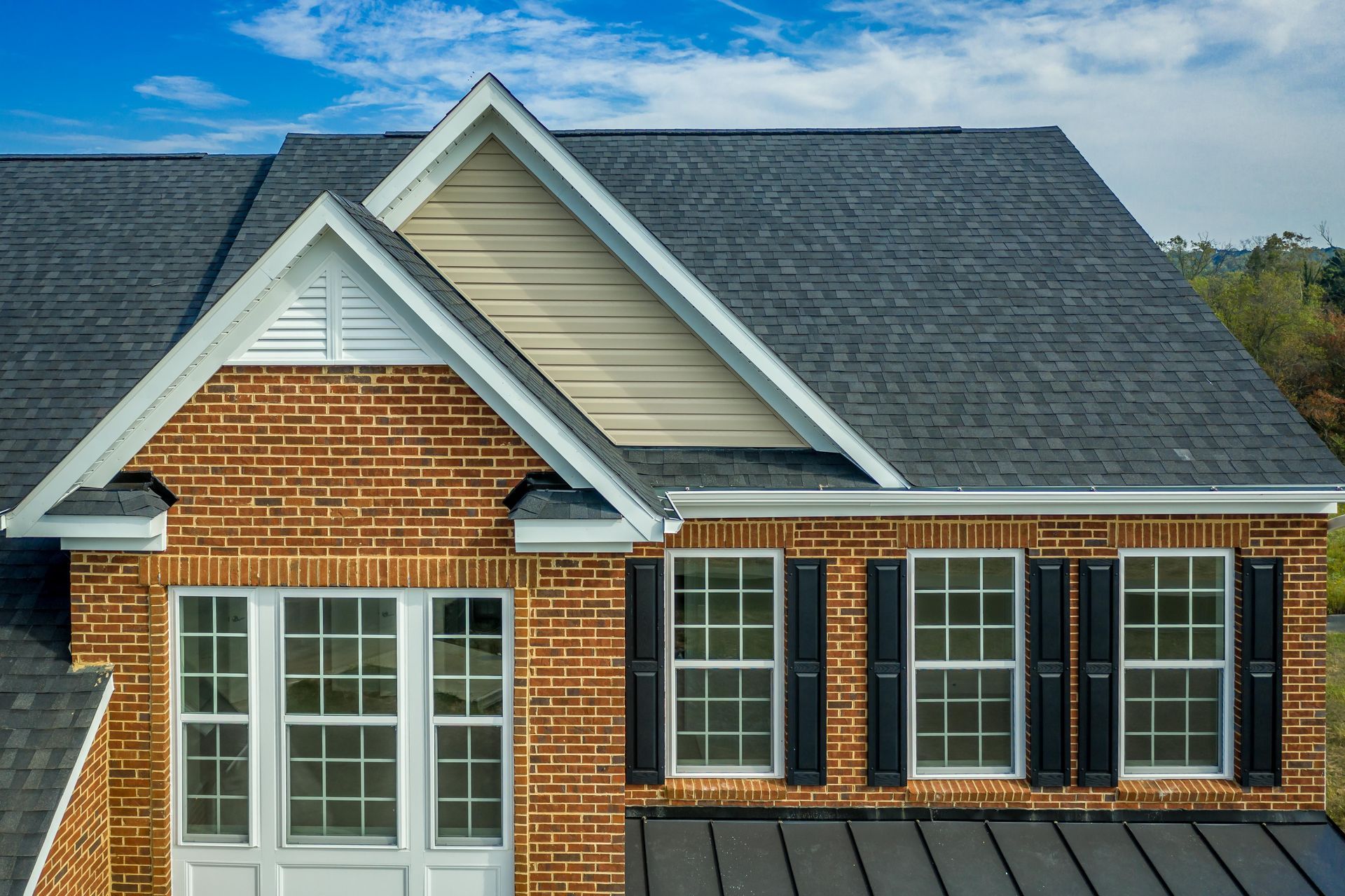 Brick house facade with white trim, black shutters, and a dark shingled roof