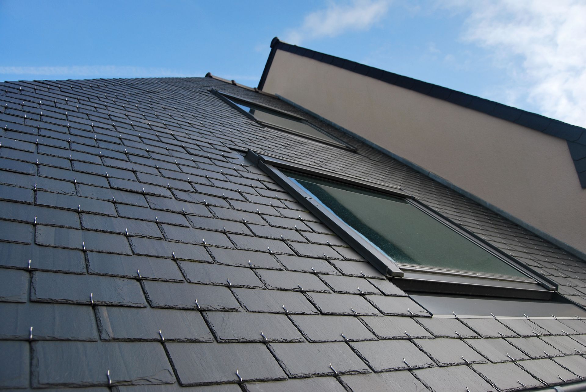 Low-angle view of a dark slate roof with skylights against a blue sky