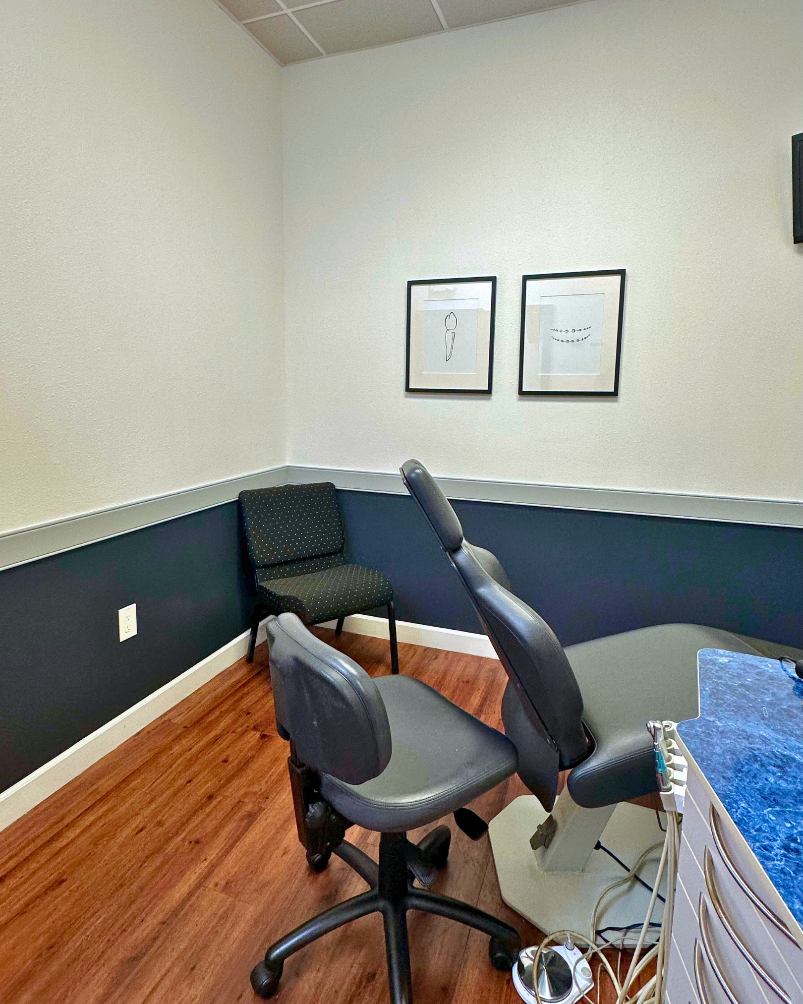 Dental office exam room with patient chair, waiting chair, and framed artwork on the wall.