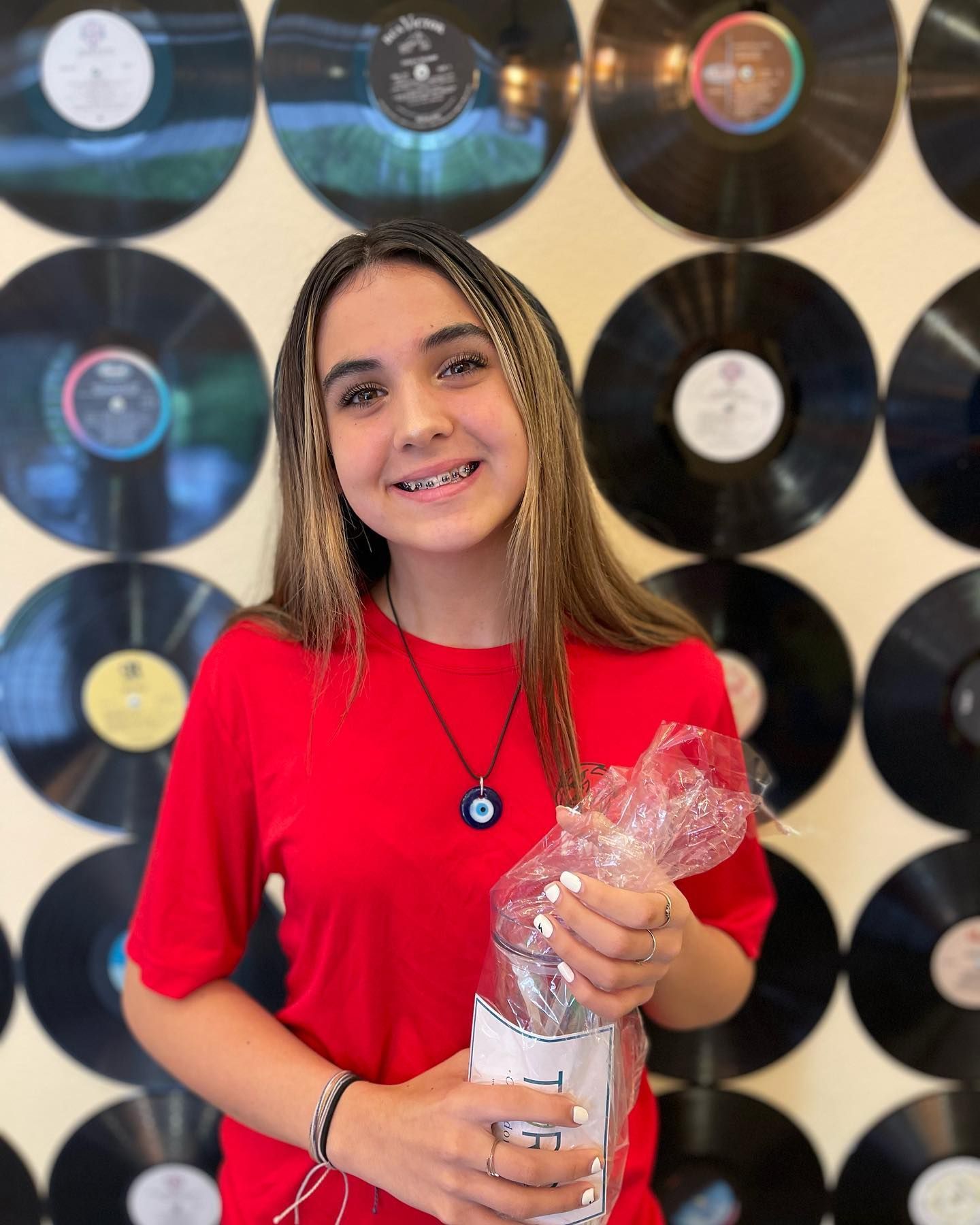 A girl in a red shirt is holding a bag in front of a wall of vinyl records.