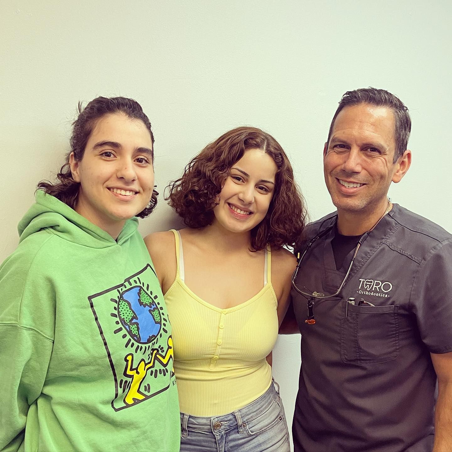 A man and two women are posing for a picture together . one of the women is wearing a green hoodie.