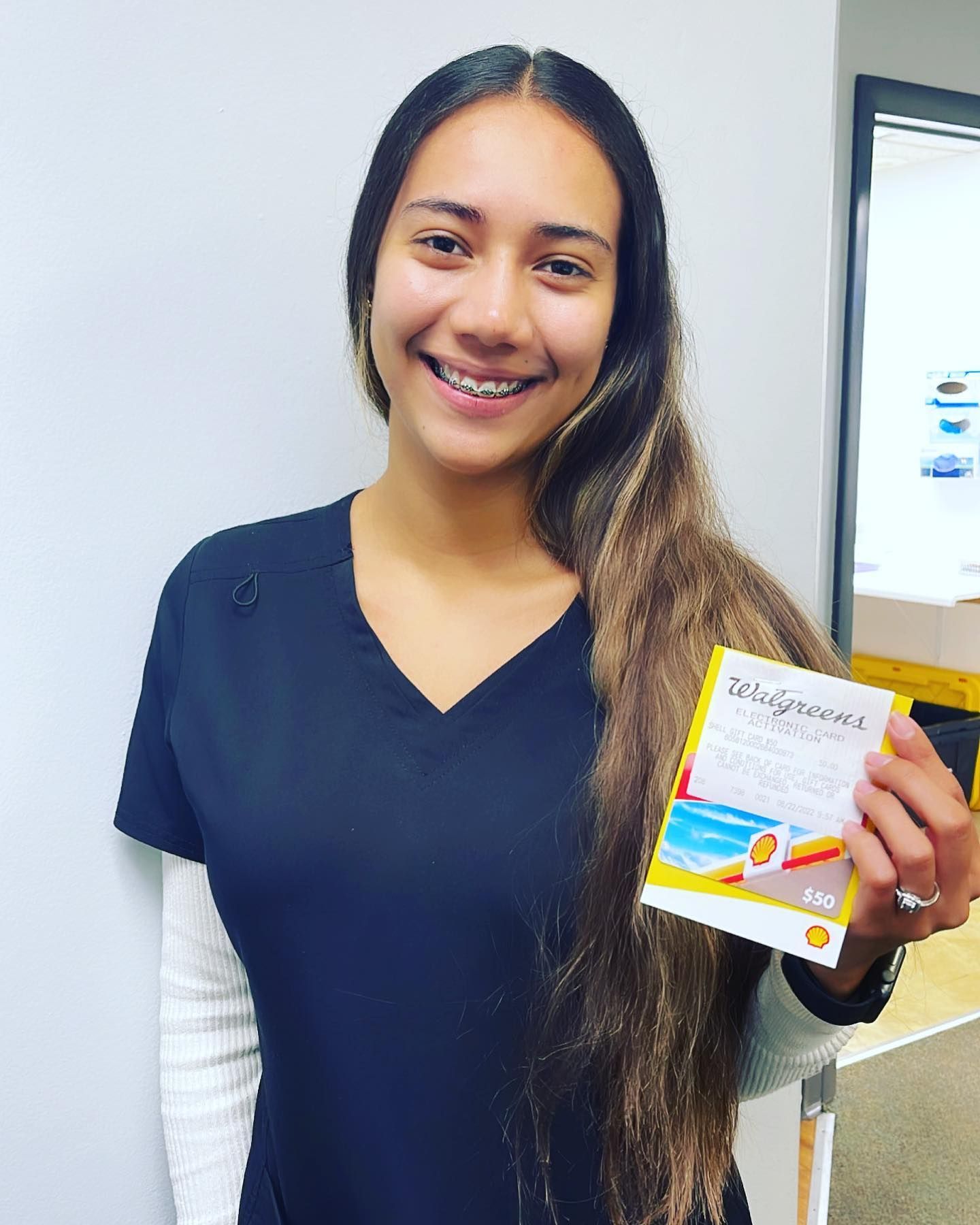 A woman in a black scrub top is holding a walgreens coupon.