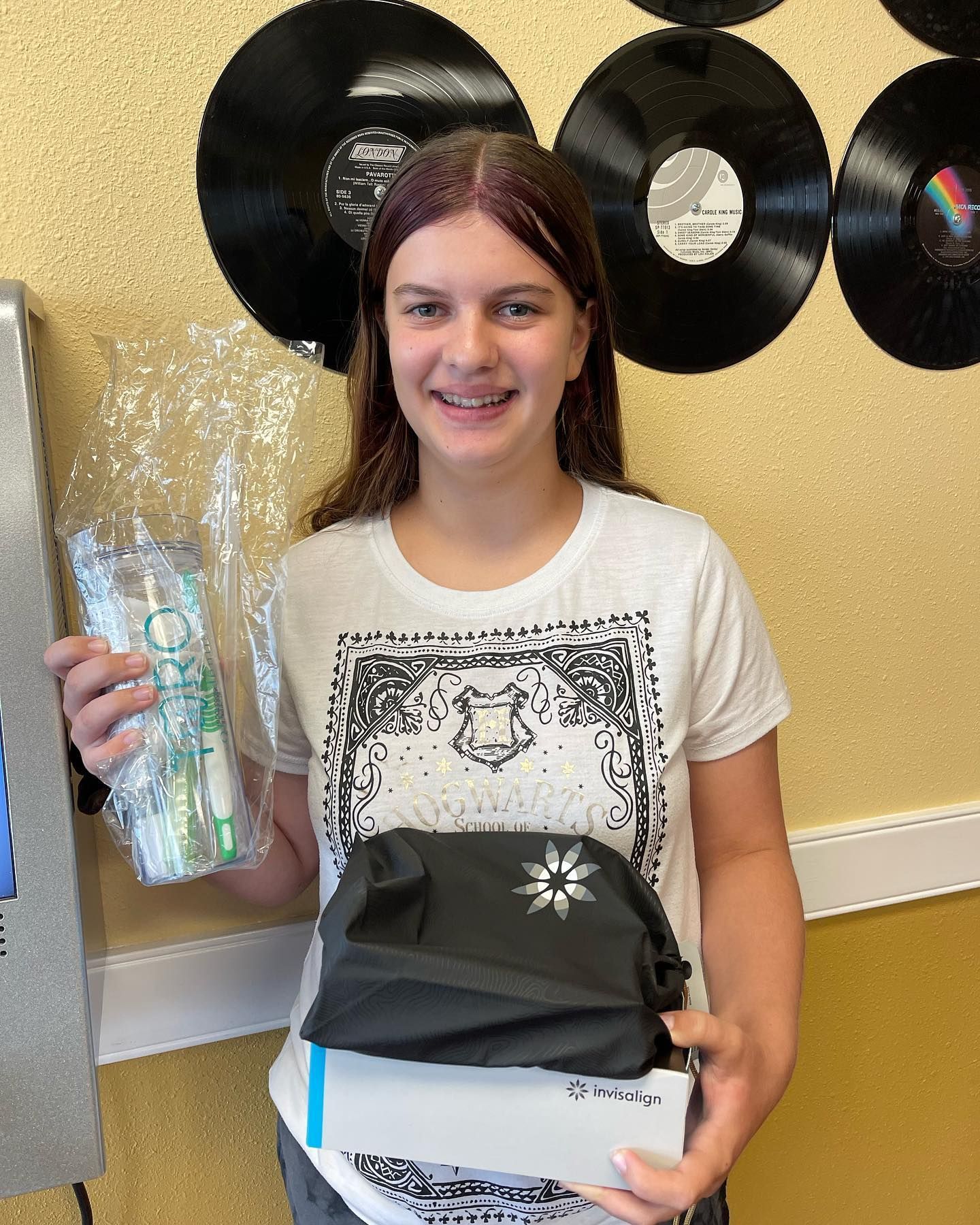 A girl in a white shirt is holding a toothbrush and a bag.