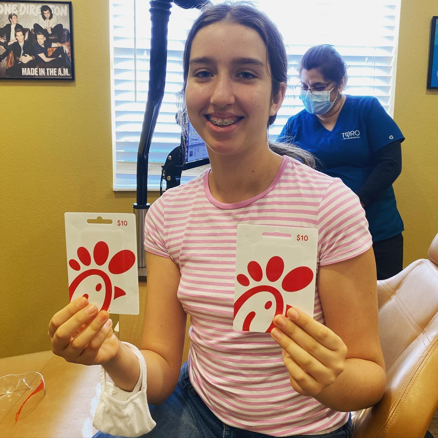 A woman in a pink striped shirt is holding two chick-fil-a gift cards