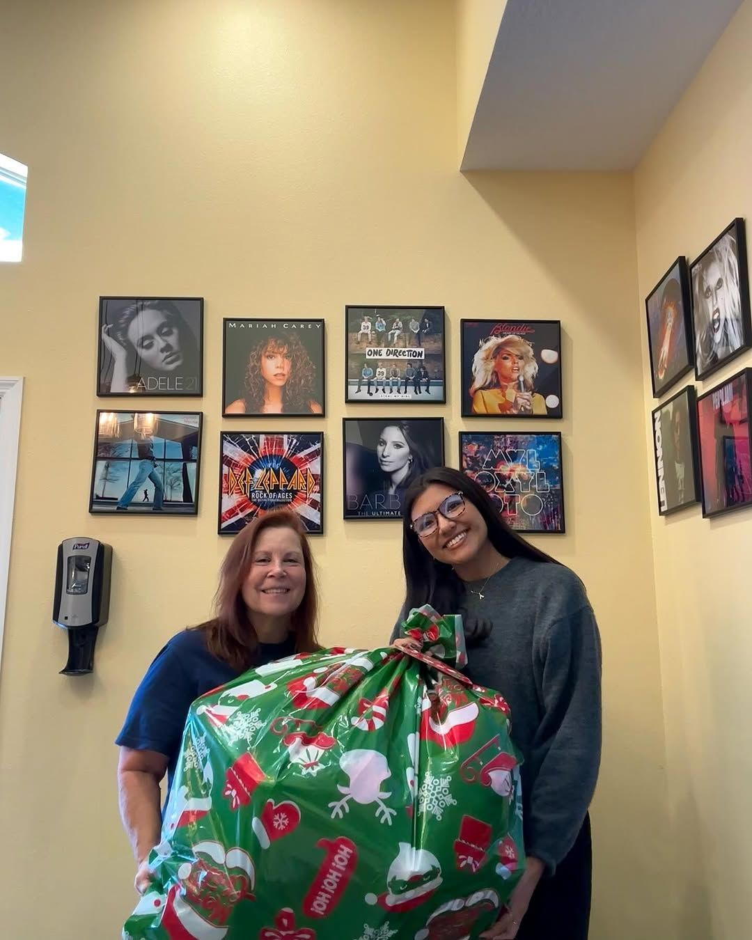Two women are standing next to each other holding a large christmas present.