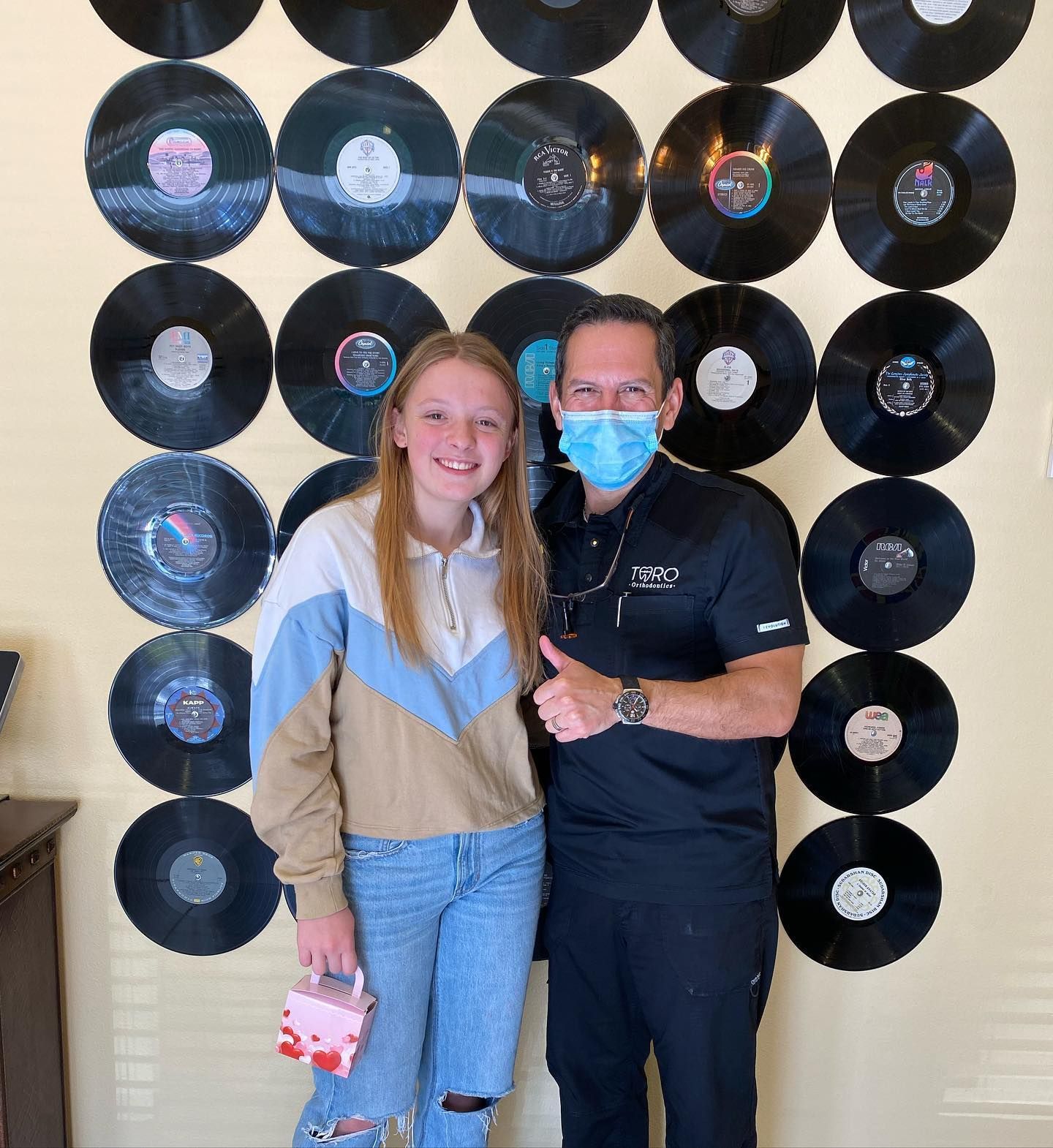 A man and a girl are posing for a picture in front of a wall of vinyl records.