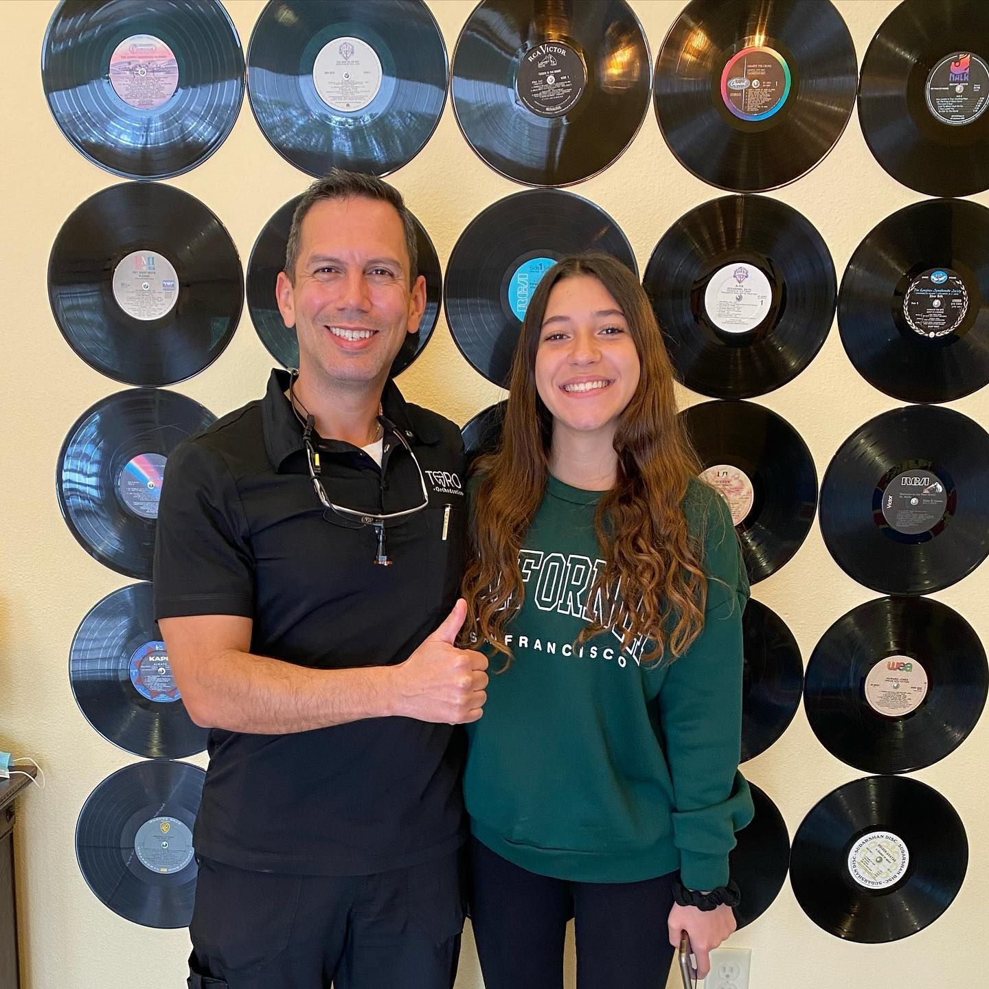 A man and a woman are posing for a picture in front of a wall of vinyl records.