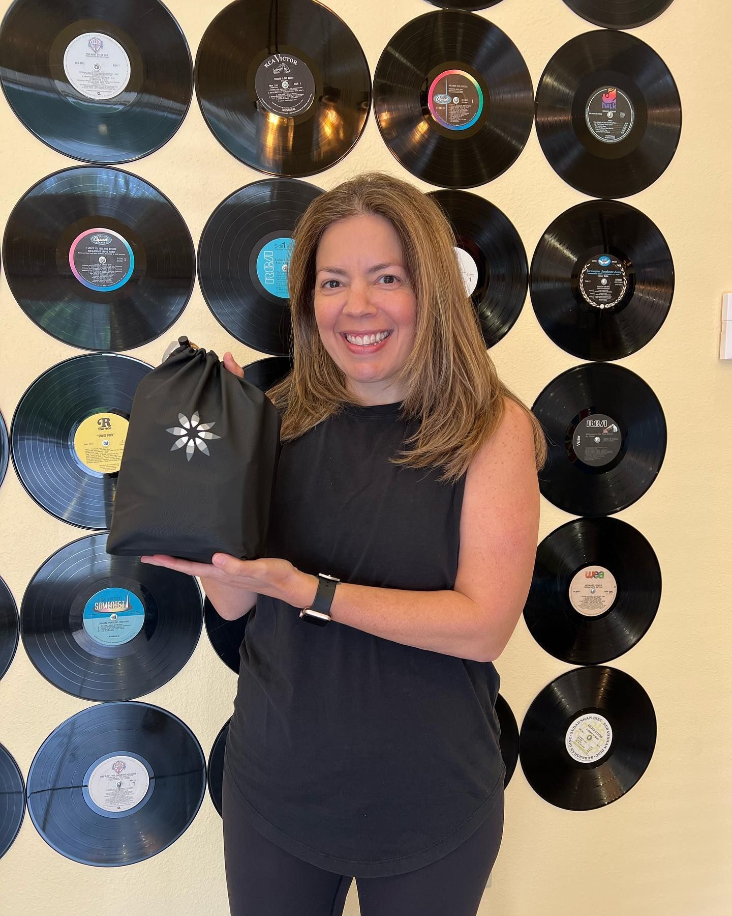 A woman is holding a bag in front of a wall of vinyl records.