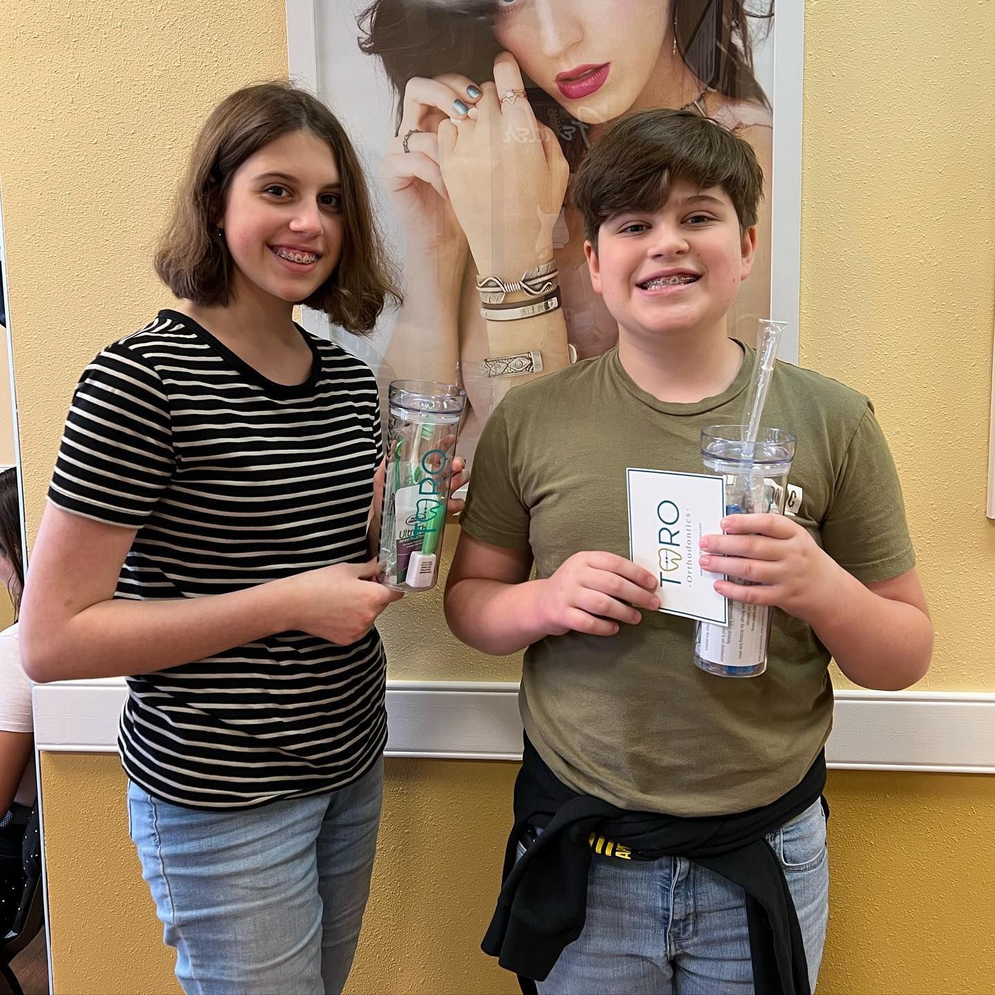 A boy and a girl are standing next to each other in front of a picture of a woman.