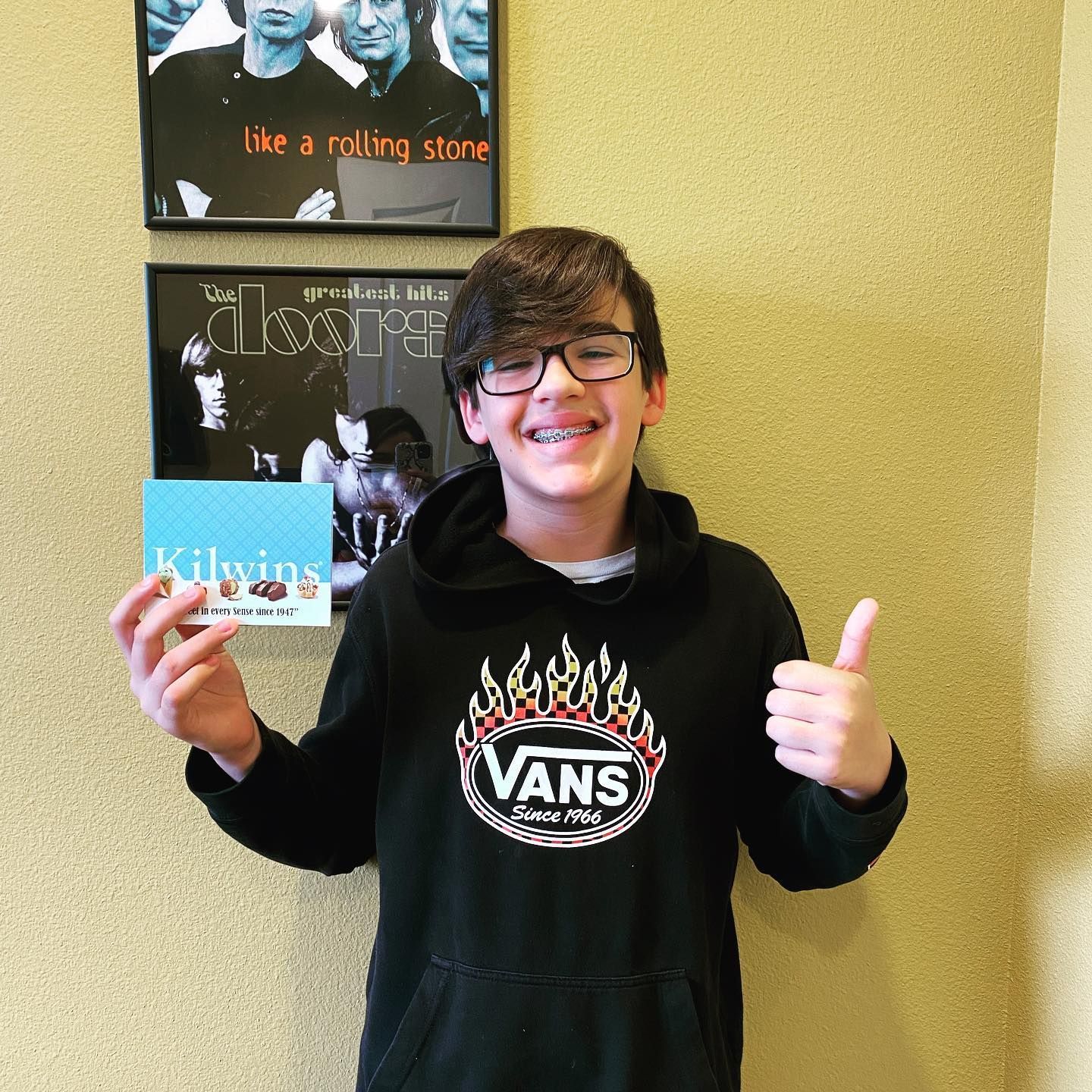 A young boy wearing a black vans sweatshirt is giving a thumbs up