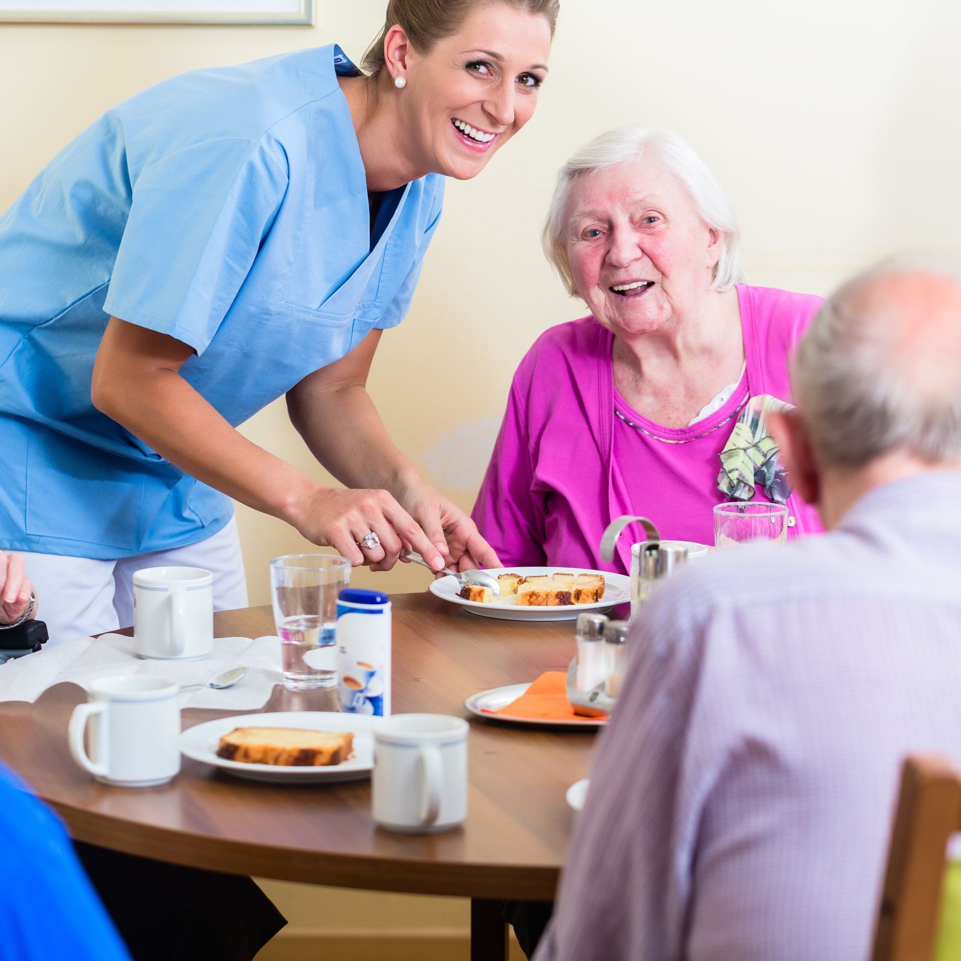A nurse is serving food to a group of people sitting at a table.