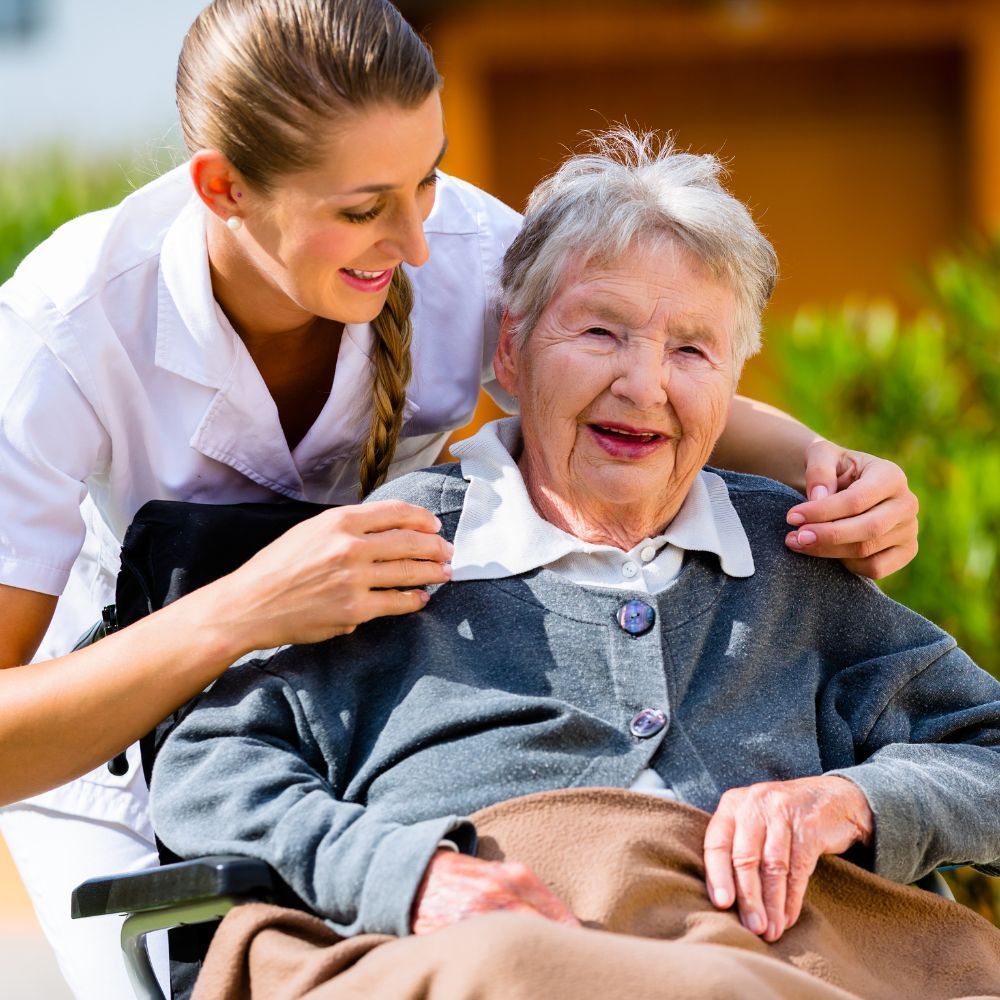 An elderly woman in a wheelchair is being helped by a nurse