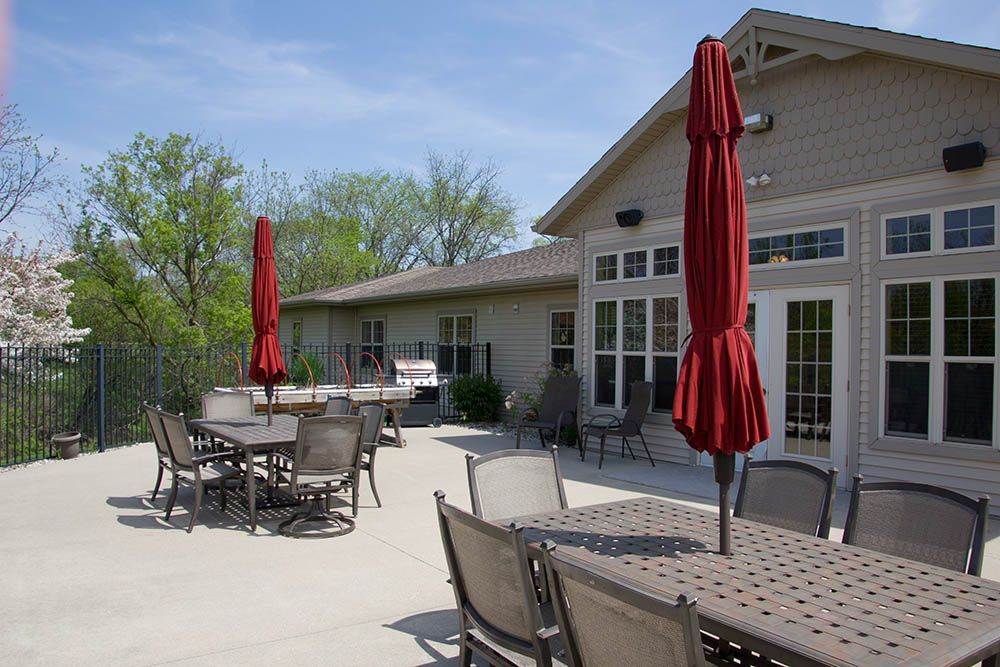 A patio with tables and chairs and red umbrellas in front of a house