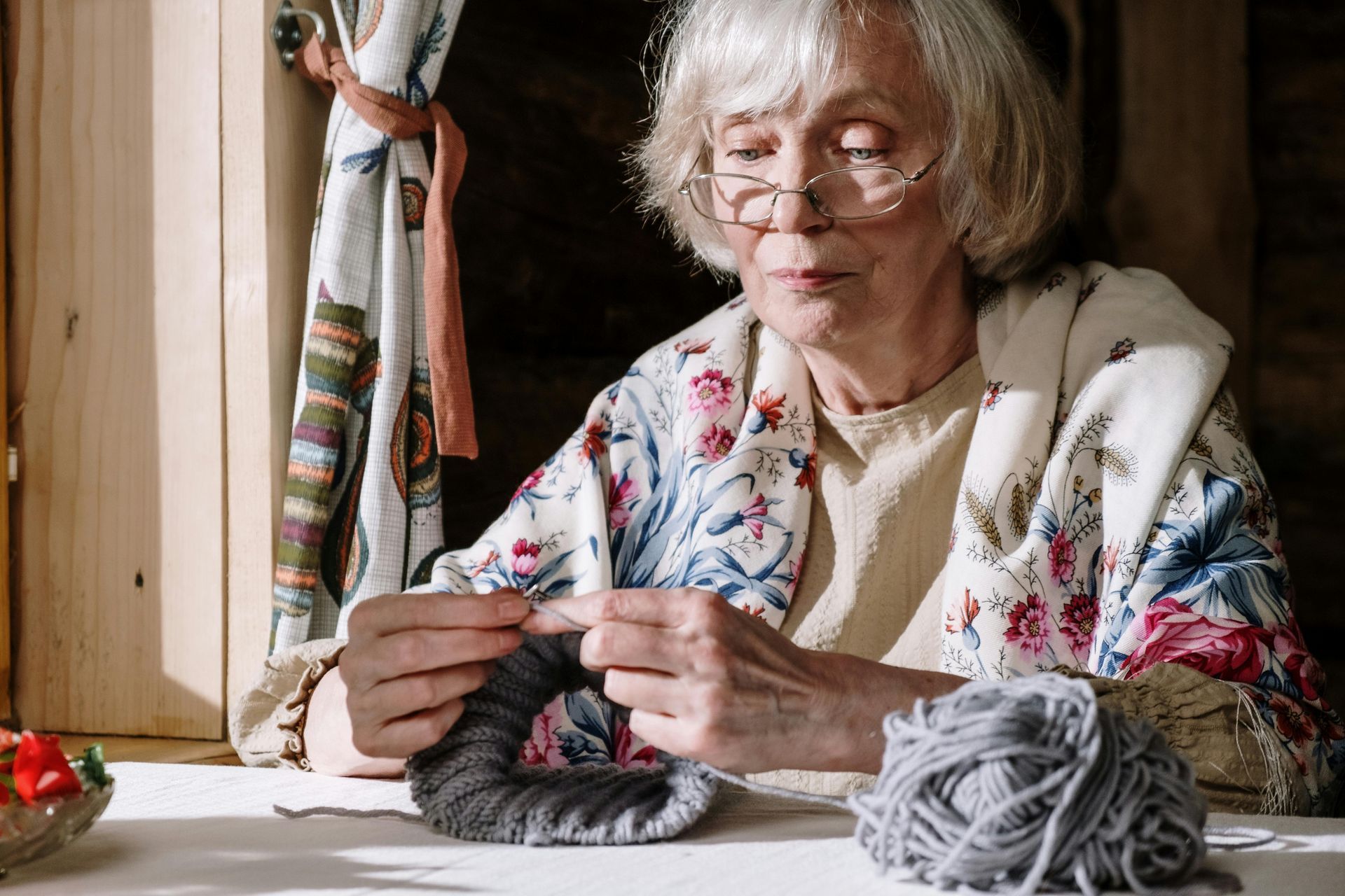 An elderly woman is sitting at a table knitting a wreath.