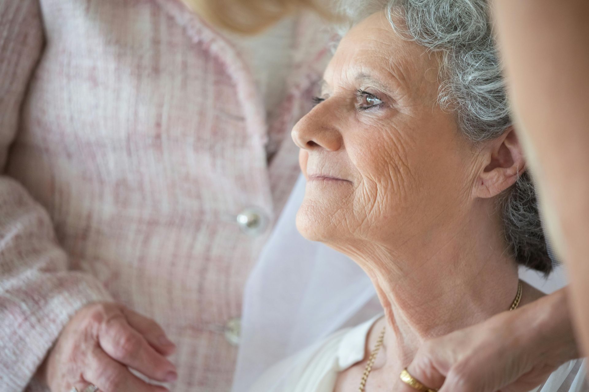 A woman is putting a necklace on an older woman 's neck.