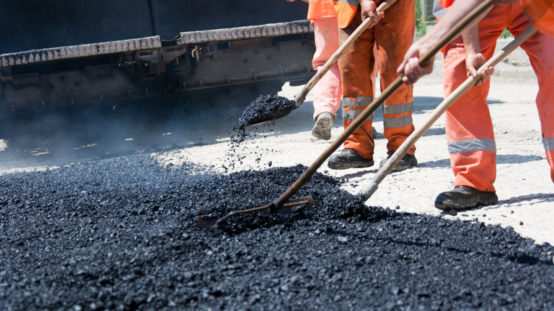 A group of construction workers are spreading asphalt on a road.