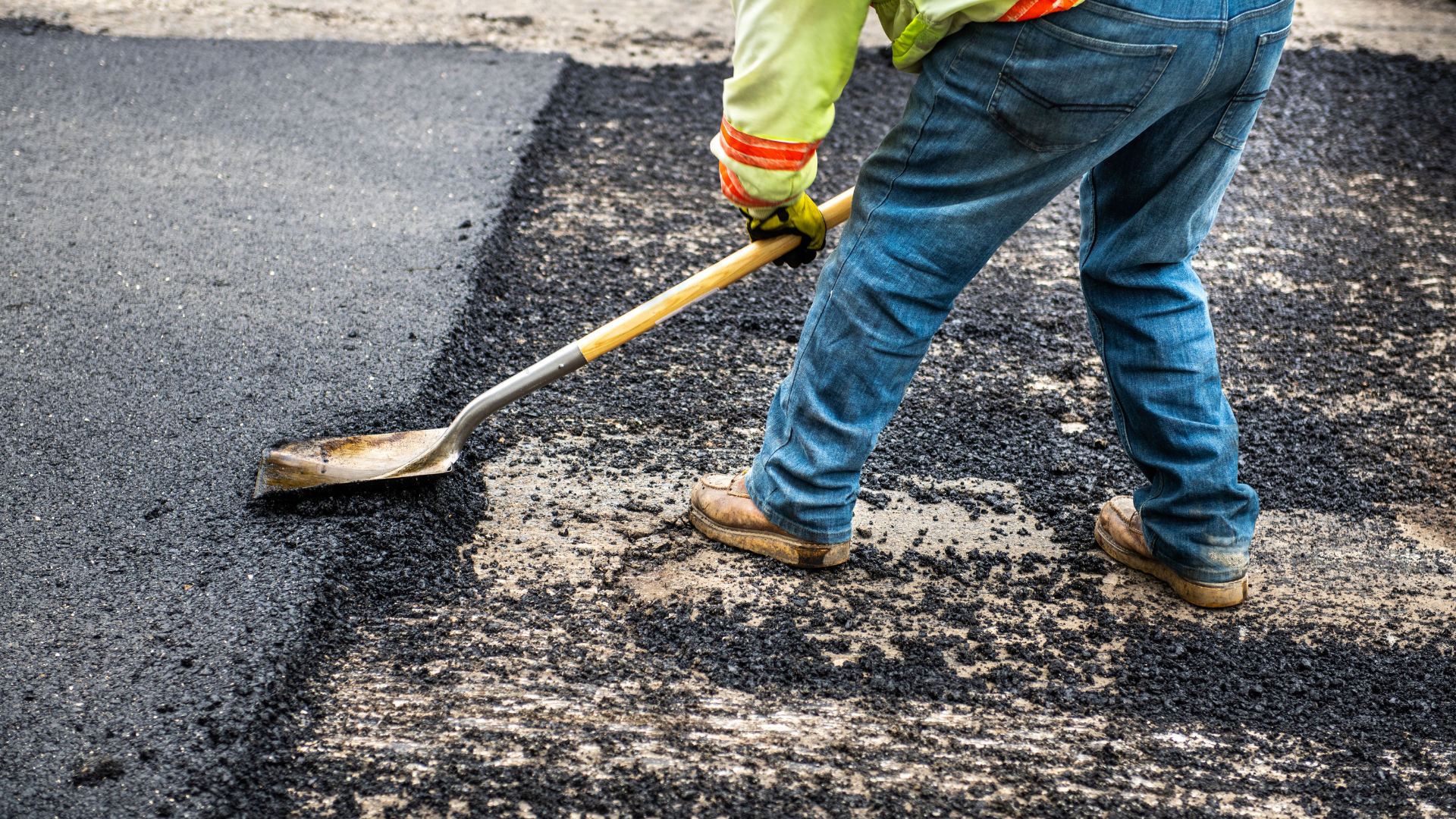 A man is spreading asphalt with a shovel and broom.