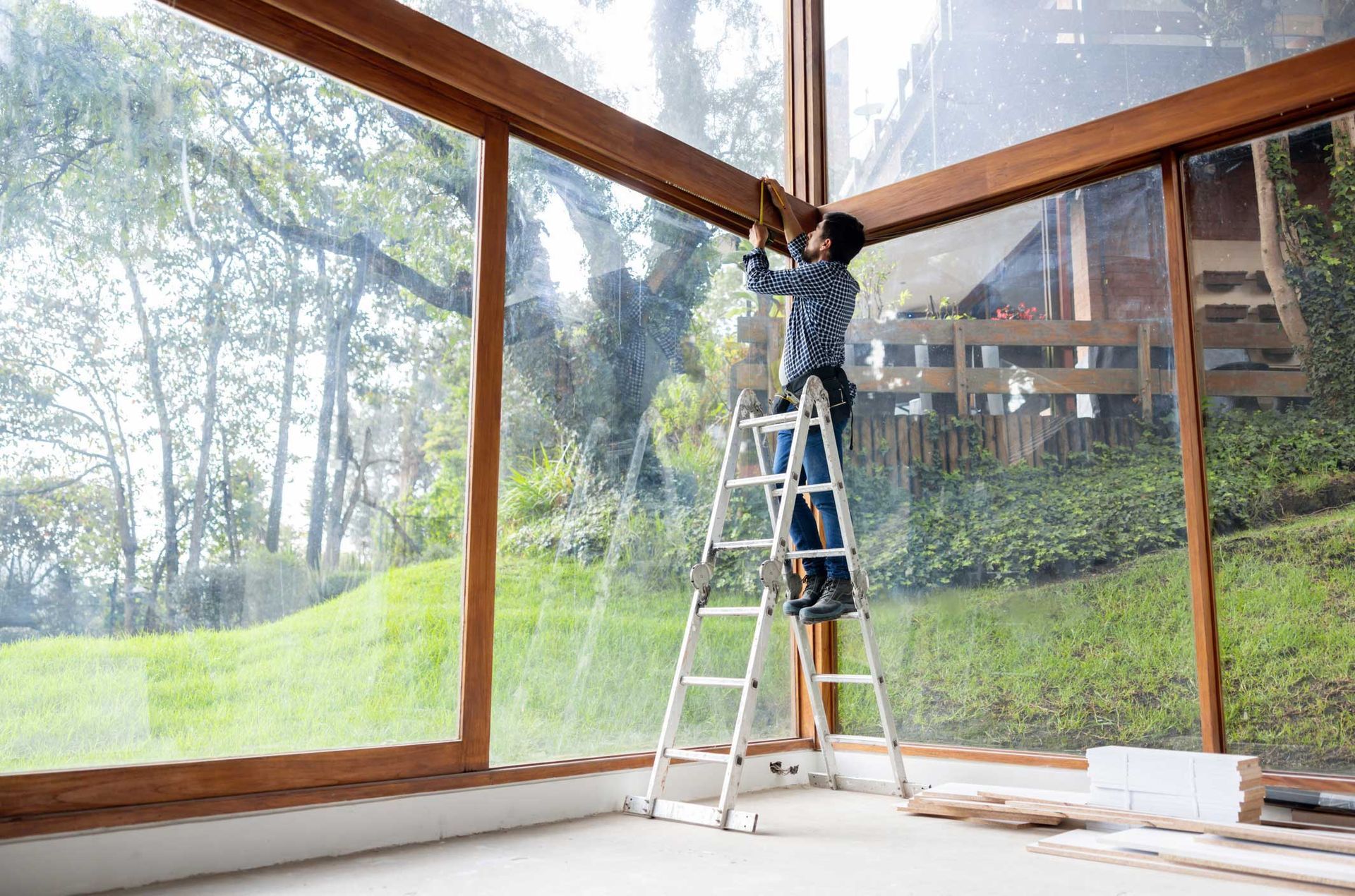 A man is standing on a ladder in front of a large window.
