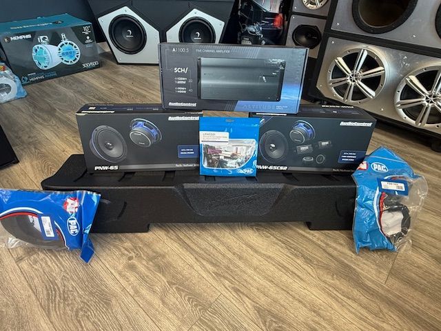 Audio equipment on a wooden floor, including speakers, amplifier, wiring, and a black speaker box.