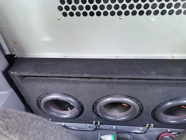 Three car subwoofers in a black box, with a metal grill above.