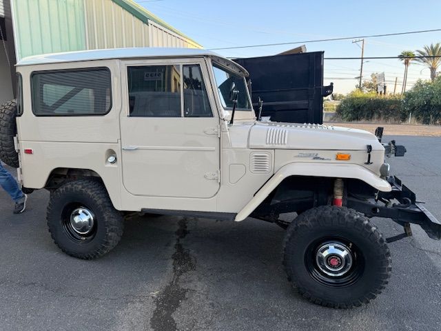 Tan Toyota Land Cruiser SUV with black wheels and a spare tire, parked outside.