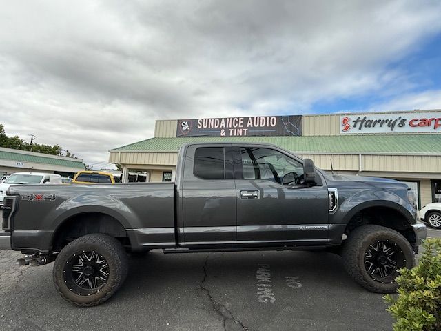 Gray Ford pickup truck with black wheels parked in front of Sundance Audio & Tint and Harry's Carpet stores.