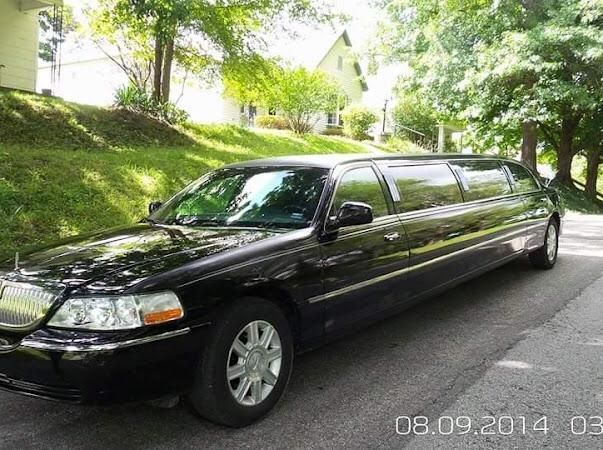 Black stretch limousine parked on a tree-lined residential street.