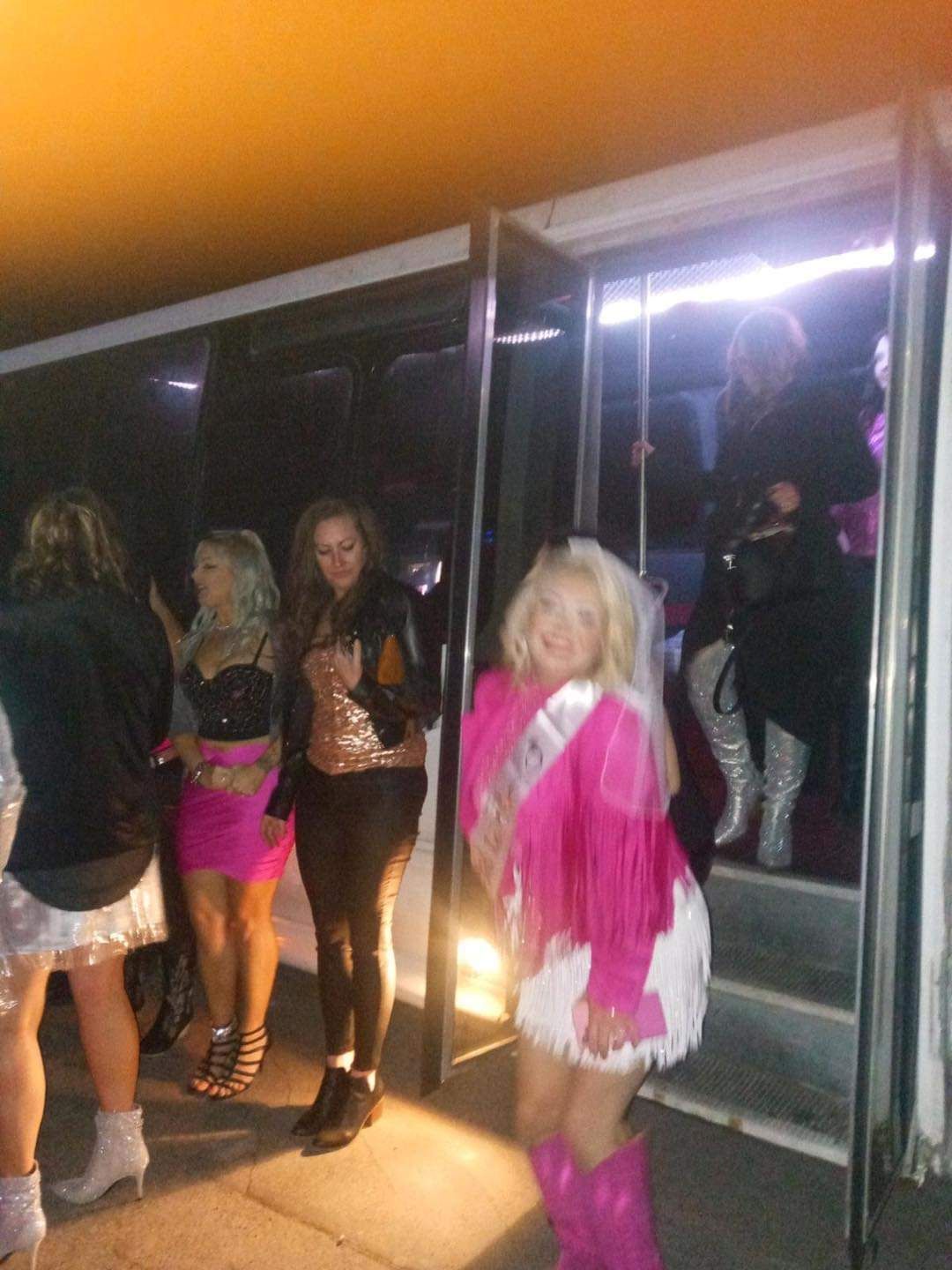 People posing outside a club entrance, one in a pink and white outfit in front.