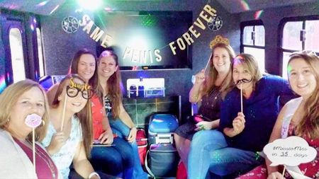 Group of friends posing inside a decorated party bus with neon lights and “Friends Forever” sign