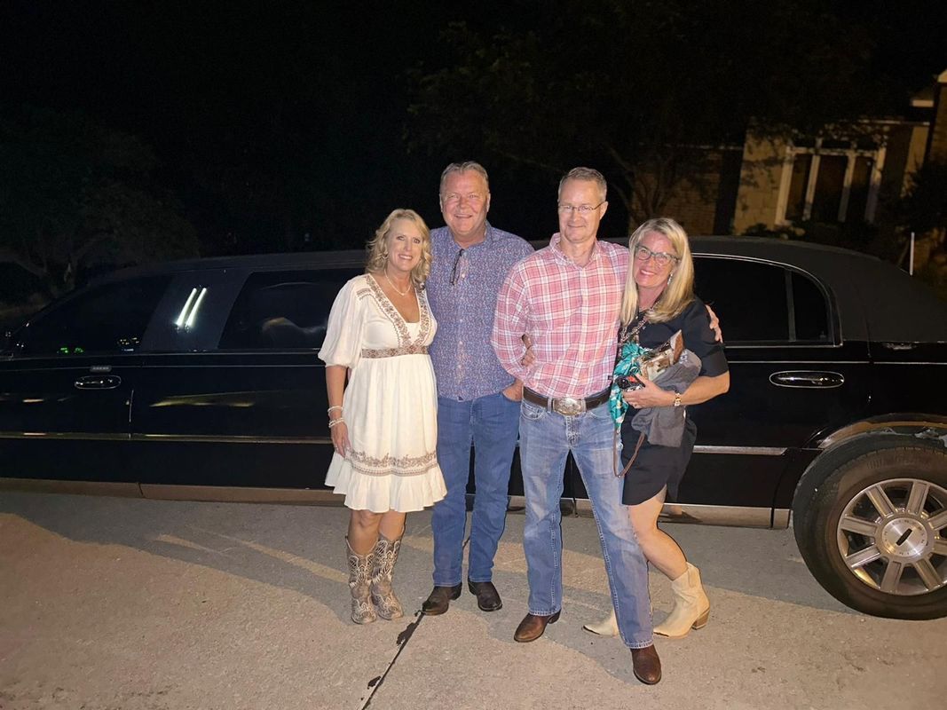 Four people posing beside a black limousine at night.