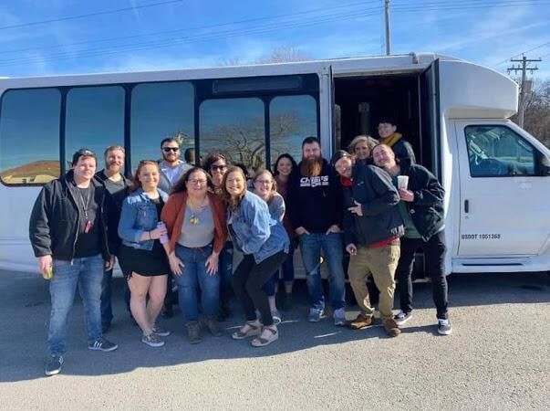 Group of people posing beside a white van on a sunny street.