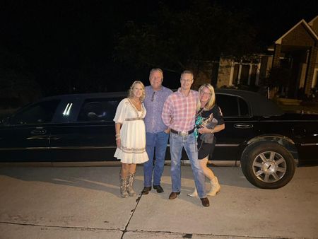 Four people standing on a driveway beside a black stretch limousine at night