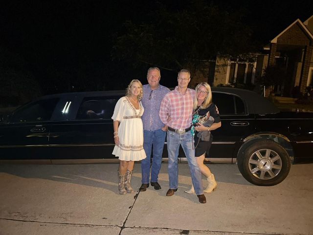 Four people standing on a driveway beside a black stretch limousine at night